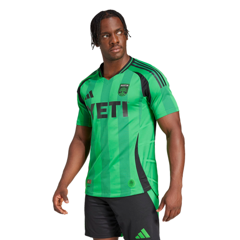A man models a green Austin FC soccer jersey with a black YETI sponsor logo and black shorts against a white background.