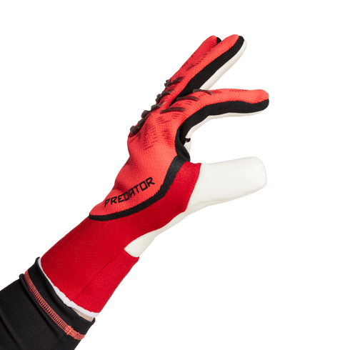 Red and black Adidas Predator goalkeeper glove shown from a side profile against a solid green background.