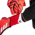 Close-up of a person putting on red Adidas Predator goalkeeper gloves, showing the textured grip and white brand logo.