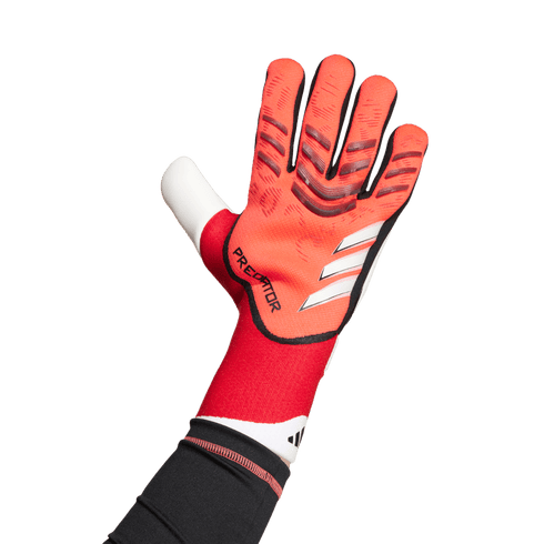 An Adidas Predator goalkeeper glove in red and white, worn on a hand against a solid green background.