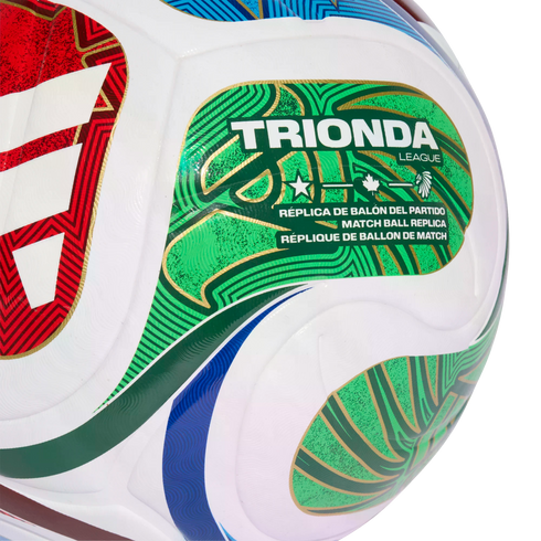 Close-up of a Trionda League replica soccer ball with green, gold, and red graphics. The ball features multilingual text and icons including a star, maple leaf, and eagle head.