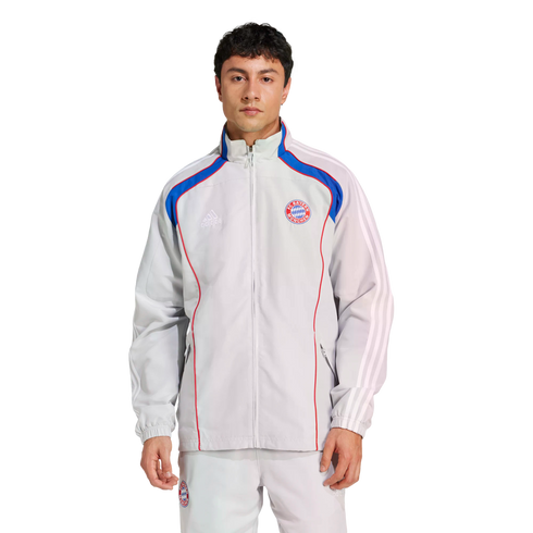 Man wearing a light gray Adidas FC Bayern Munich tracksuit with blue and red accents against a white background.