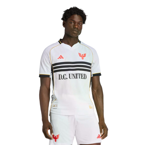 A man wearing a white D.C. United soccer jersey with three black chest stripes, red bird crests, and matching white shorts against a solid black background.
