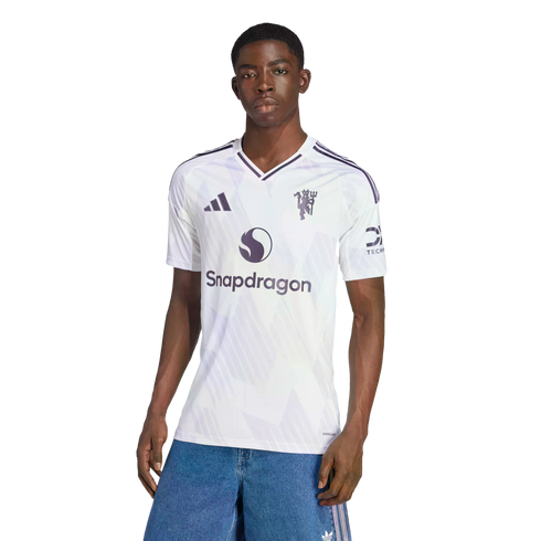 A man modeling a white Manchester United soccer jersey with a Snapdragon logo, posed against a black background.