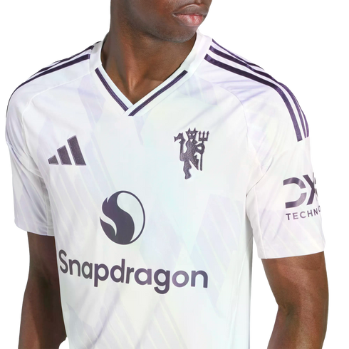 A person wearing a white Manchester United football jersey with purple accents, featuring the club crest, Adidas logo, and Snapdragon sponsor.