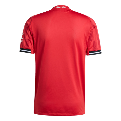 Rear view of a textured red football jersey with "Theatre of Dreams" on the collar and black-and-white striped cuffs, set against a black background.
