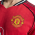 Close-up of a red Manchester United football jersey featuring the team's yellow and red crest on the chest, with black shoulder stripes and patterned fabric.