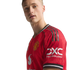 A blonde man wearing a red Manchester United football jersey with the club crest and sponsor logos against a black background.