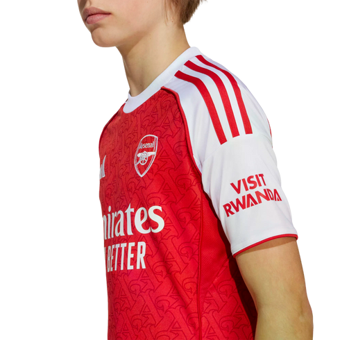 Side profile of a person wearing a red and white Arsenal FC home football jersey with the club crest and sponsors visible against a white background.