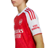 Side profile of a person wearing a red and white Arsenal FC home football jersey with the club crest and sponsors visible against a white background.