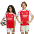 Two children in Arsenal FC home kits; a girl holds a football, and a boy stands with hands on hips. Both smile against a plain white background.