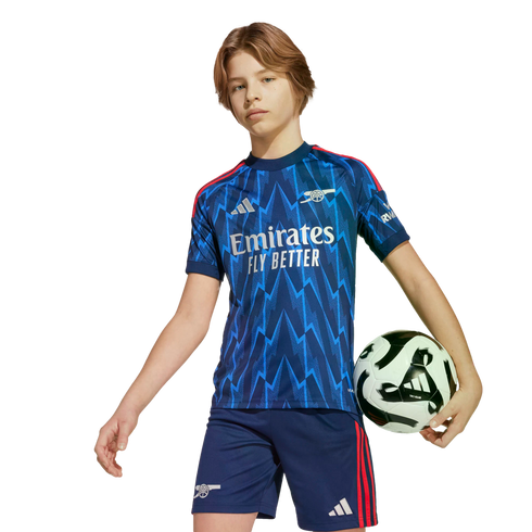 A young person wearing a blue Arsenal soccer kit with a lightning bolt pattern, holding a soccer ball under their arm against a black background.