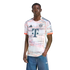 Young Black man modeling a white FC Bayern Munich jersey with a red and grey abstract pattern and blue denim shorts against a white background.