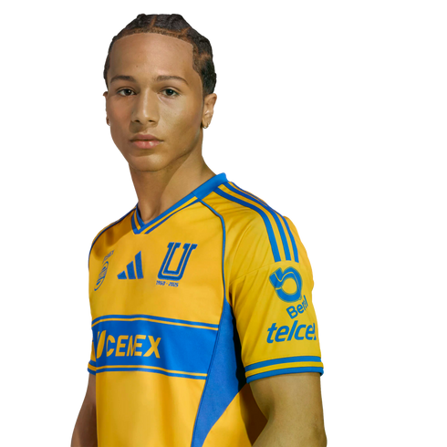 A young man with braided hair wearing a yellow and blue Tigres UANL soccer jersey with sponsor logos, set against a plain white background.