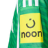 Close-up of a green striped sports jersey sleeve featuring a yellow patch with the black "noon" logo and brand icon.