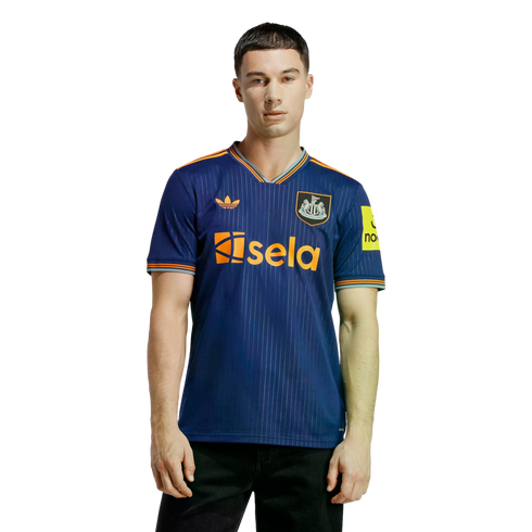 A man models a navy blue Newcastle United soccer jersey with orange trim, featuring thin vertical stripes, the Sela sponsor logo, and Adidas trefoil logo, against a black background.