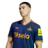 A young man wearing a navy blue Newcastle United football jersey with orange trim and "sela" sponsor logo, set against a black background.