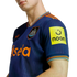 A person wears a blue Newcastle United football jersey with orange accents, featuring the club crest, the "Sela" sponsor on the front, and the "noon" logo on the sleeve.