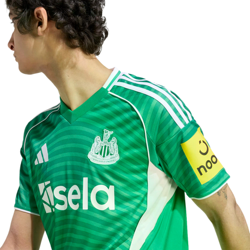 Person in a green Newcastle United football jersey with white Adidas stripes and Sela sponsor logo, shown in profile against a black background.