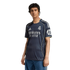 A young man wearing a navy blue Real Madrid soccer jersey with yellow trim and blue jeans, standing against a plain white background.