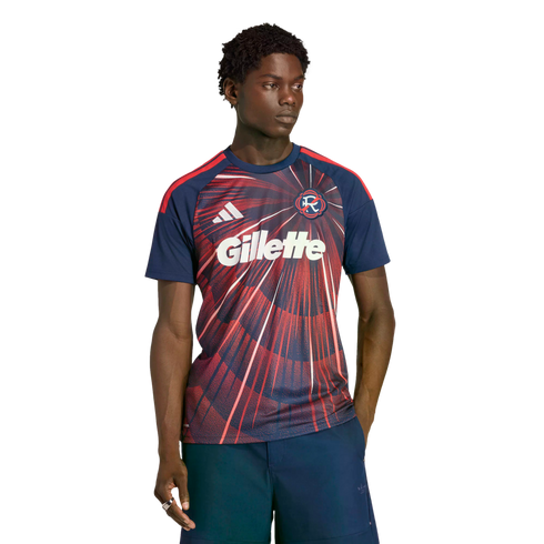A man wearing a navy and red Adidas soccer jersey with a large white Gillette logo and dark shorts, posed against a black background.