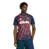 A man wearing a navy and red Adidas soccer jersey with a large white Gillette logo and dark shorts, posed against a black background.