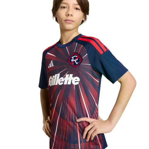 A young person wearing a New England Revolution soccer jersey with a red sunburst pattern and Gillette sponsor logo, posing against a solid black background.