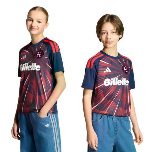 Two children pose in matching navy and red soccer jerseys and blue denim Adidas pants against a black background.