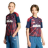 Two children pose in matching navy and red soccer jerseys and blue denim Adidas pants against a black background.