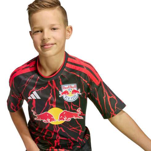 A young boy smiling while wearing a black and red New York Red Bulls soccer jersey.