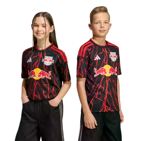 A young girl and boy pose in black New York Red Bulls soccer jerseys with red lightning patterns against a solid black background.