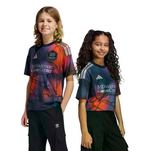 Two smiling children posing in vibrant Houston Dynamo FC soccer jerseys against a black background.