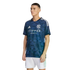 A man models a navy blue NYCFC soccer jersey with a geometric pattern, Adidas logo, and Etihad sponsor, paired with white shorts against a black background.