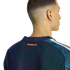Back view of a man wearing a navy New York City FC soccer jersey with orange text below the collar. The shoulders have a blue geometric pattern and white stripes.