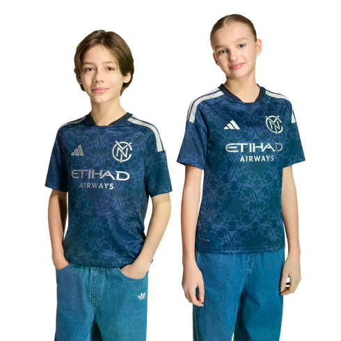 Two children wear matching navy patterned New York City FC soccer jerseys with silver Etihad Airways logos and blue jeans, standing against a black background.