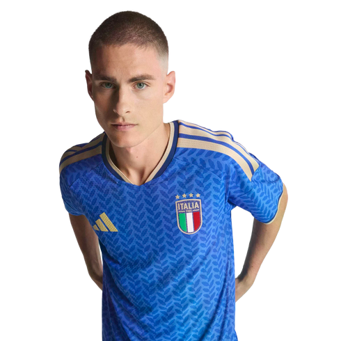 A man wearing a blue Italy national soccer team jersey with gold accents against a black background.