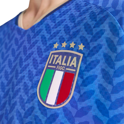 Close-up of a blue Italy national soccer jersey featuring the FIGC crest with four gold stars and a textured leaf pattern.