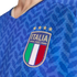 Close-up of a blue Italy national soccer jersey featuring the FIGC crest with four gold stars and a textured leaf pattern.