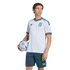 A man poses in a white Italy soccer jersey and blue shorts, holding a football against a black background.
