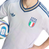 Close-up of a person in a light blue Adidas Italy football jersey with the FIGC crest, holding a FIFA soccer ball against a black background.