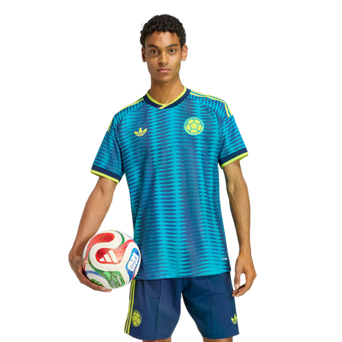 A man in a blue and teal patterned soccer jersey and matching shorts holds a colorful soccer ball against a solid black background.