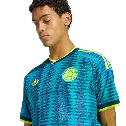 Young man wearing a blue and yellow Colombia soccer jersey with a wavy pattern, looking down against a black background.