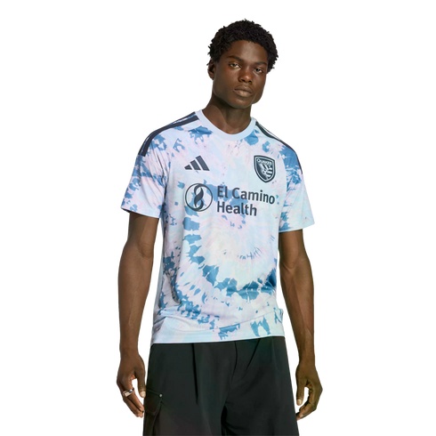 A man wearing a light blue and pink tie-dye San Jose Earthquakes soccer jersey with an El Camino Health logo.