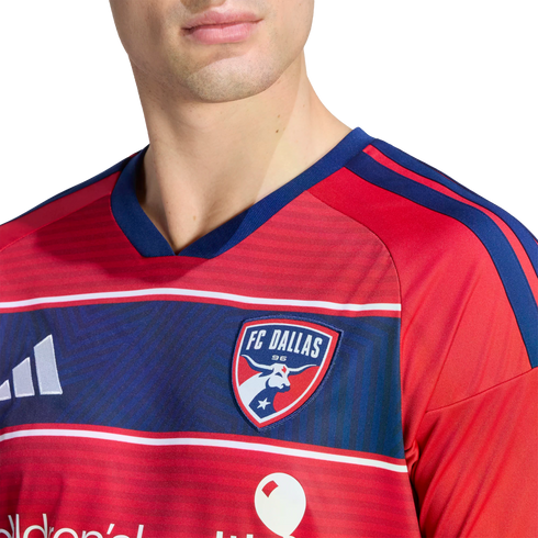 Close-up of a person wearing a red FC Dallas soccer jersey with blue horizontal stripes and the team crest on the chest.