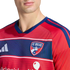Close-up of a person wearing a red FC Dallas soccer jersey with blue horizontal stripes and the team crest on the chest.