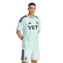 A man models a light green and white striped Austin FC soccer kit with black Adidas details and a YETI logo. He wears matching white shorts against a black background.