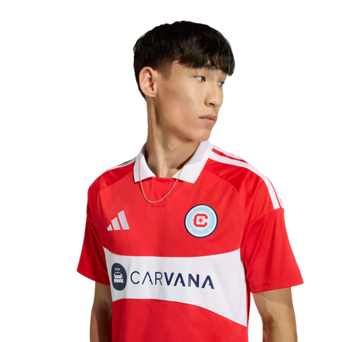 A man in a red Chicago Fire FC jersey with a white horizontal band featuring the Carvana logo. The shirt has a white collar and Adidas stripes on the shoulders.