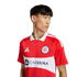 A man in a red Chicago Fire FC jersey with a white horizontal band featuring the Carvana logo. The shirt has a white collar and Adidas stripes on the shoulders.