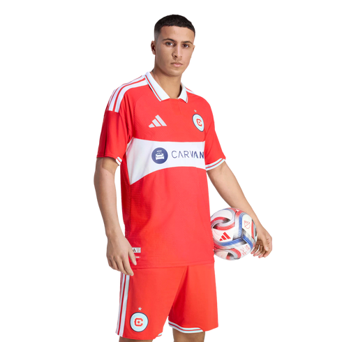 A male soccer player in a red Chicago Fire uniform holding a soccer ball against a black background.