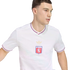 A man wearing a white Olympique Lyonnais soccer jersey with red and blue trim, looking sideways against a black background.